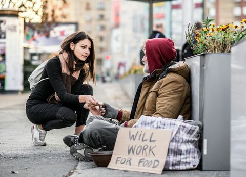 Nuori nainen antaa rahaa kodittomalle kerjäläiselle, joka istuu kaupungissa.