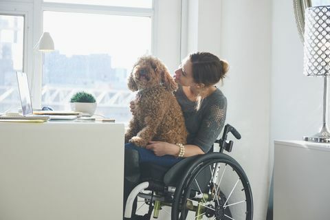 Valkoihoinen nainen pyörätuolissa koiran kanssa sylissä