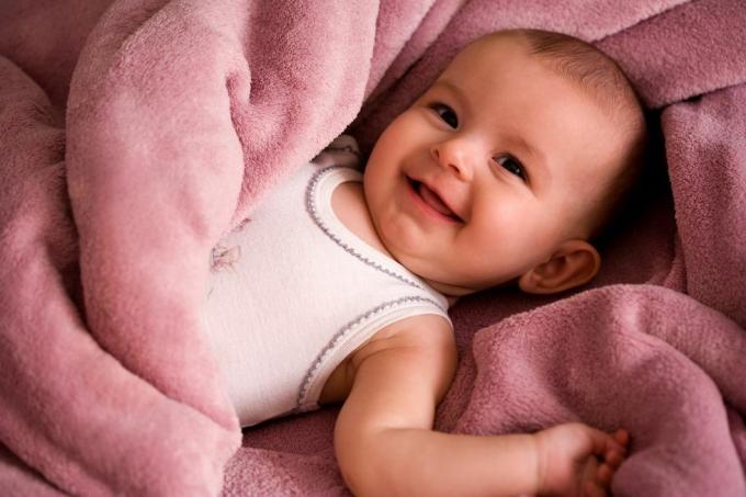 muotokuva vauvasta valkoisessa tankkityylisessä paidassa hymyilevänä ja pehmeän vaaleanpunaiseen peittoon käärittynä