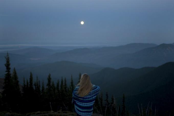 nainen käärittynä huopaan ja katselee vuoristomaisemaa täysikuulla takaa katsottuna