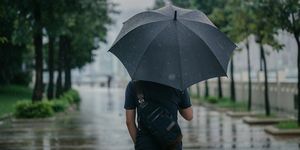 takanäkymä älykkäästä kausaalimiehestä, joka pitää sateenvarjoa ja kävelee puistoa pitkin sateisessa kaupunkikaupungissa