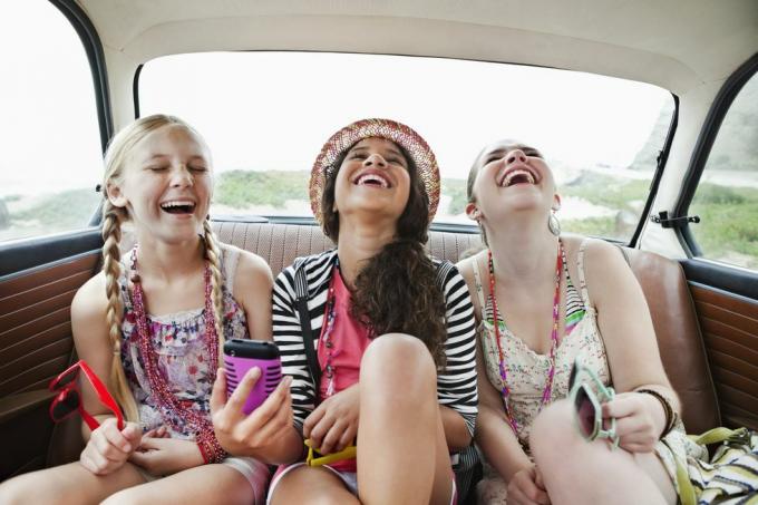 kolme tyttöä nauramassa auton takapenkillä