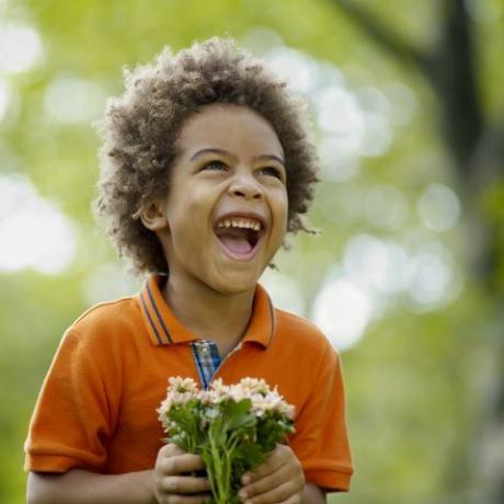 Poika (3-5) pitää kukkaa, nauraa