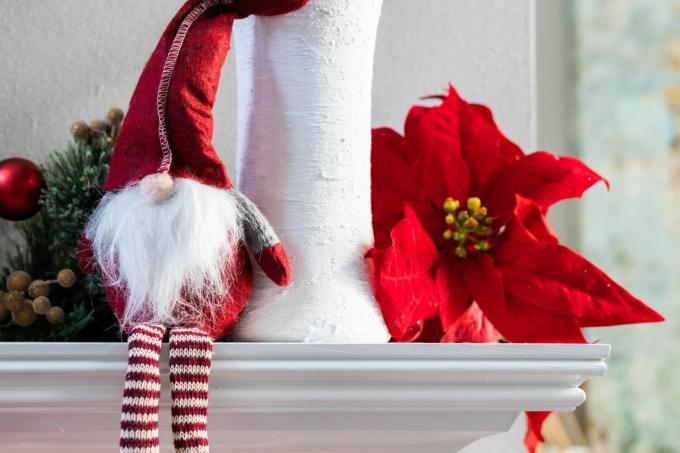 klassinen norjalainen loma joulutonttu koristelu istuu valkoisella modernilla vaipalla, jossa on valkoinen maljakko, jossa on eukalyptus ja joulutähti