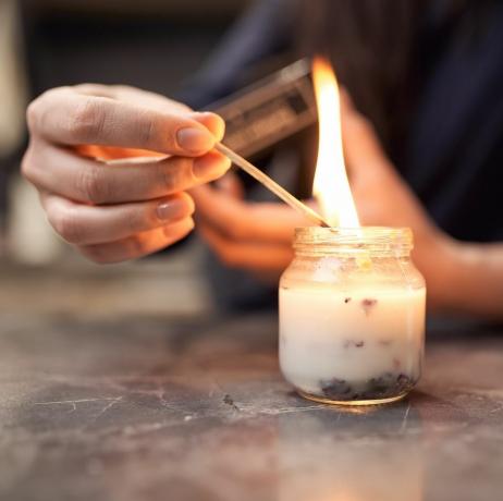 rajaa nimetön nainen palava tulitikku sytyttävä aromaattinen kynttilä lasipurkissa kotona marmoripöydälle