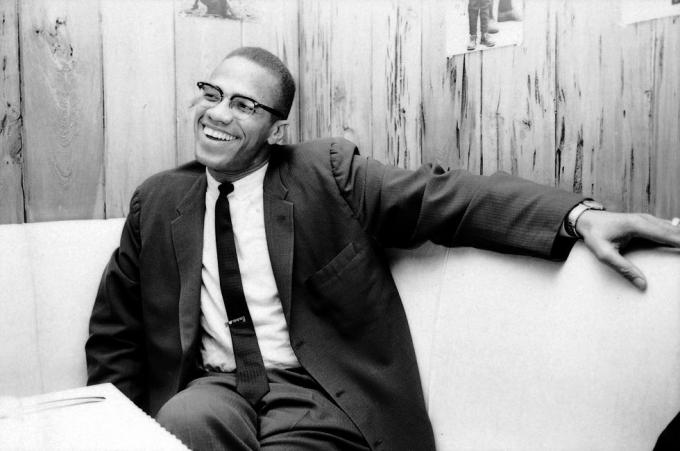 mustavalkoinen valokuva malcolm x: stä istumassa kopissa hymyillen