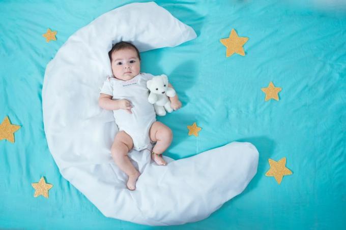 kaunis latinalainen tyttövauva, kaksi kuukautta vanha, makaa valkoisella kuun muotoisella lakanalla, jonka molemmilla puolilla on keltaisia ​​tähtiä ja sen alla sininen lakana