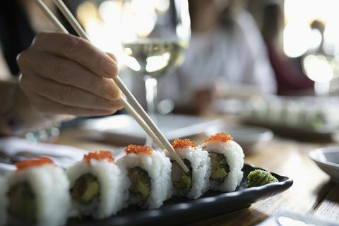 Nainen syömäpuikot tavoittavat sushi ravintolan tarjotin