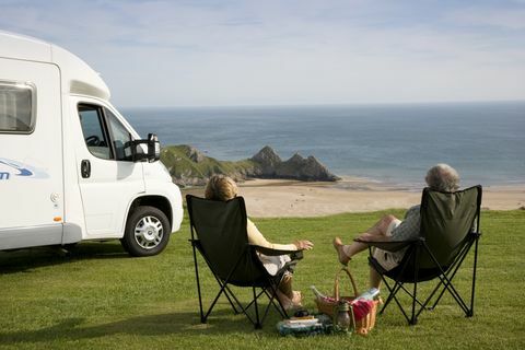 Pari piknikillä rentouttavassa tuolissa matkailuautonsa vieressä nauttien näkymästä kolmella Cliffs Bayllä Gowerin niemimaalla Walesissa., Three Cliffs Bay, Swansea, Wales.