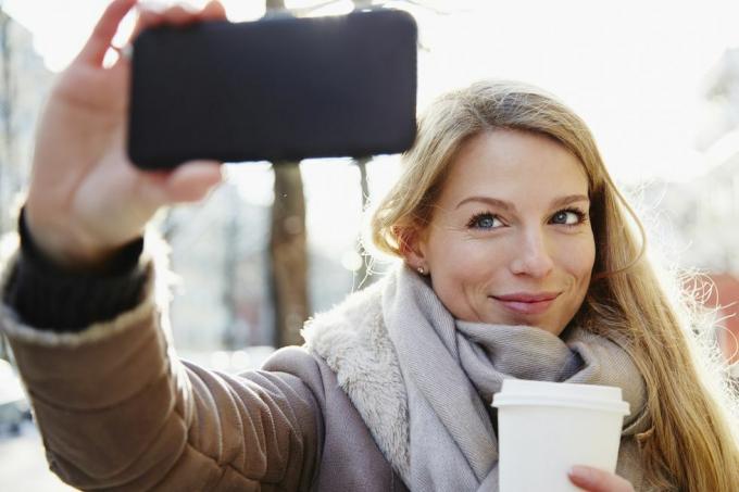 komea nainen kävelee kaupungin kaduilla talvella, ottaa selfien ja pitää kahvia mukana, taustavalaistu