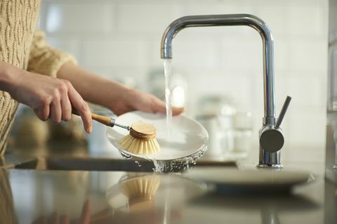 nainen käyttää muovitonta harjaa astioiden puhdistamiseen tiskialtaan läheltä