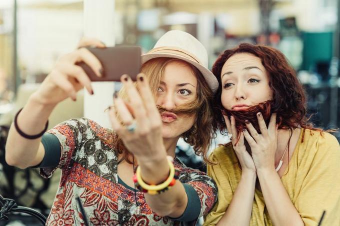 kaksi tyttöystävää pitelevät hiuksia kasvoillaan näyttämään parta ja viikset ja ottavat niistä selfien
