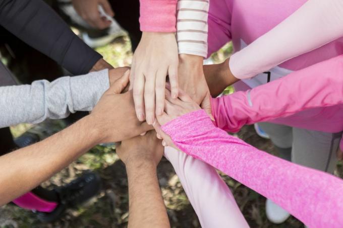 ryhmä ihmisiä, jotka käyttävät vaaleanpunaisia ​​paitoja kädet yhdessä yhtenäisyydessä