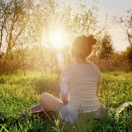 nuori nainen istuu joogaasennossa nauttien auringonlaskusta luonnossa