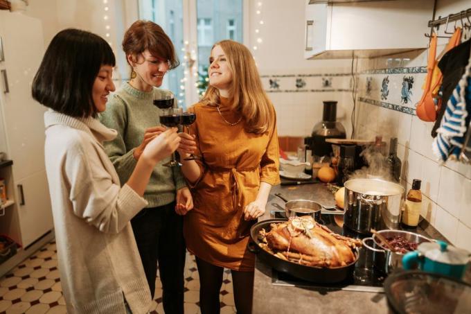 kolme naista juomassa punaviiniä valmistaessaan kalkkuna-ateriaa kotona kalkkunan kanssa ja kolme kattilaa liedellä