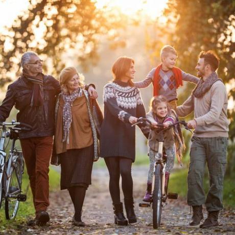 hymyilevä usean sukupolven perhe kävelemässä polkupyörien kanssa luonnossa ja nauttimassa yhteisestä ajastaan