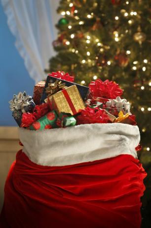 joulupukin kassi täynnä värikkäitä pakattuja lahjoja joulukuusen edessä
